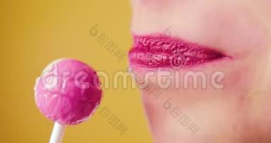 一个嘴唇粉红色的女人甜美地舔一个棒棒糖，喜欢吃糖果。 黄色背景，微笑，有趣，工作室，